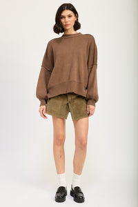 Woman wearing a brown sweater and green shorts on a white background