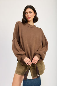 Woman wearing a brown oversized sweater with green shorts on a white background
