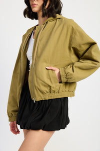 Person wearing a green jacket over a white shirt and black shorts on a white background