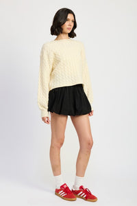 Woman wearing a light yellow sweater, black skirt, white socks, and red sneakers on a white background